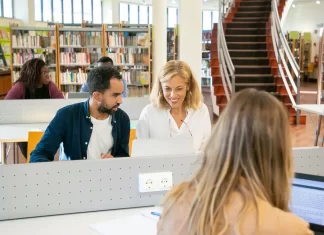 Międzynarodowa grupa studentów pracuje przy laptopach w bibliotece kampusu.